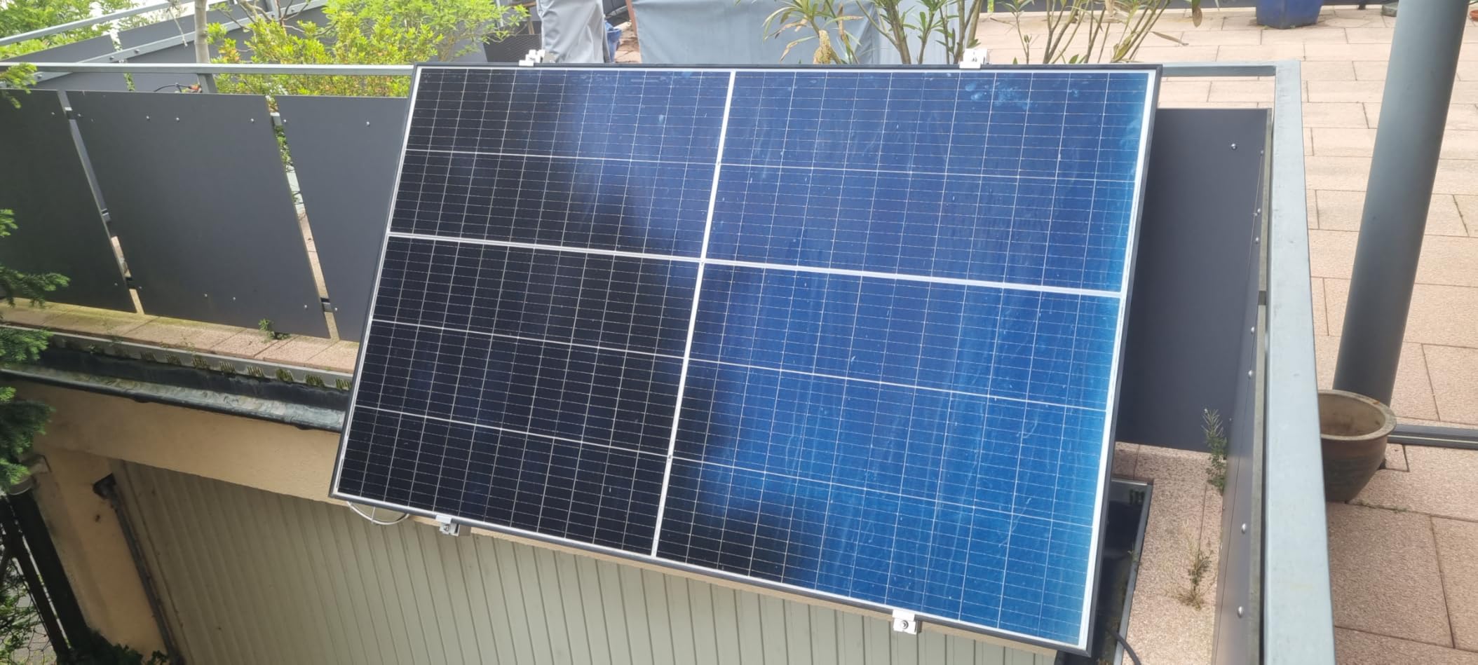 Solarmodul mit Klemmhalterung außen an einem Metall-Balkongeländer befestigt, sonniger Tag auf einer Dachterrasse