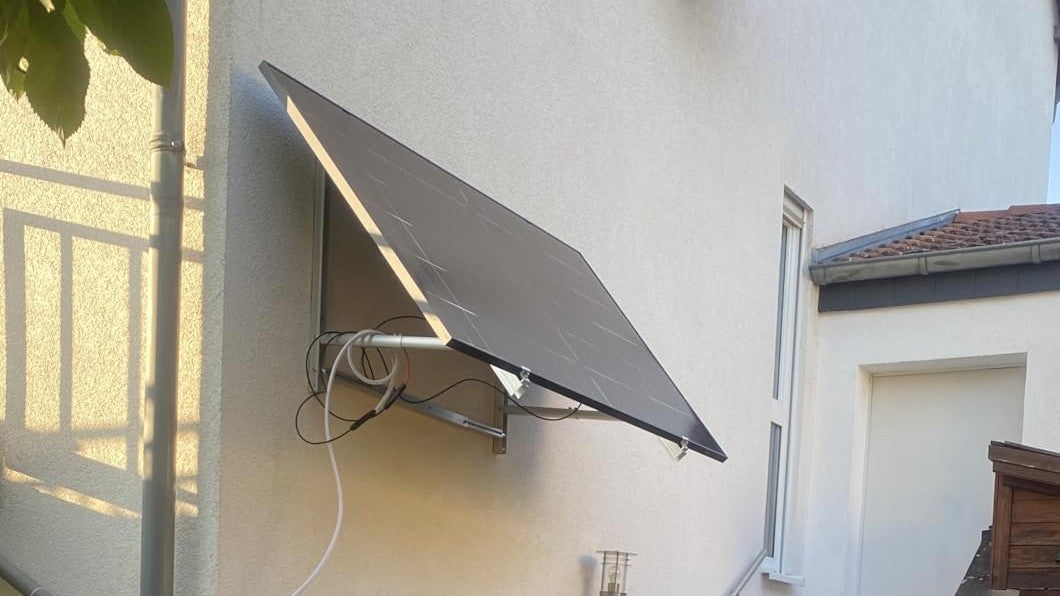 Fertig montiertes Balkonkraftwerk mit Wandhalterung an einer weißen Putzwand, Modul angewinkelt zur Sonne